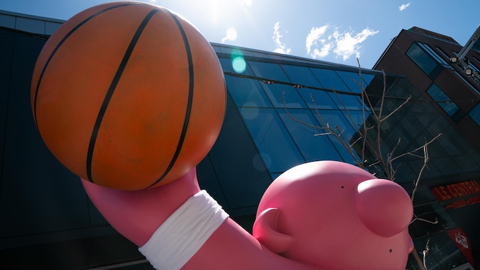 Une sculpture rose porte un ballon de basketball au ciel.