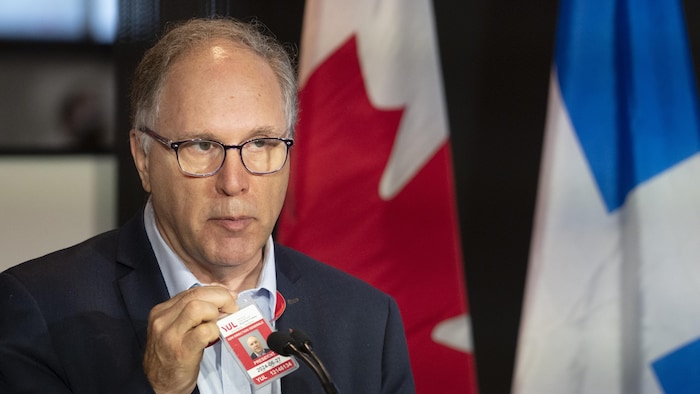 فيليب رينفيل متحدثاً في مؤتمر صحفي وخلفه علما كندا وكيبيك.