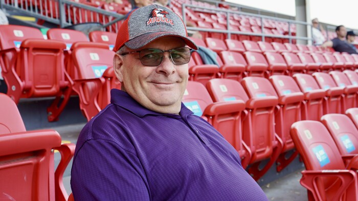 Un homme portant une casquette des Aigles de Trois-Rivières est assis dans les gradins d’un stade.