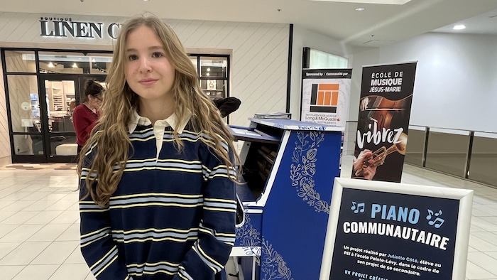 Une adolescente pose à coté d'un piano dans le corridor d'un centre d'achat.