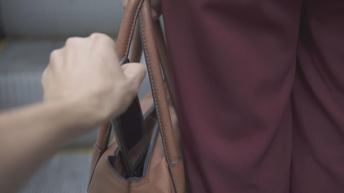 Un pickpocket vole un téléphone d'un sac.