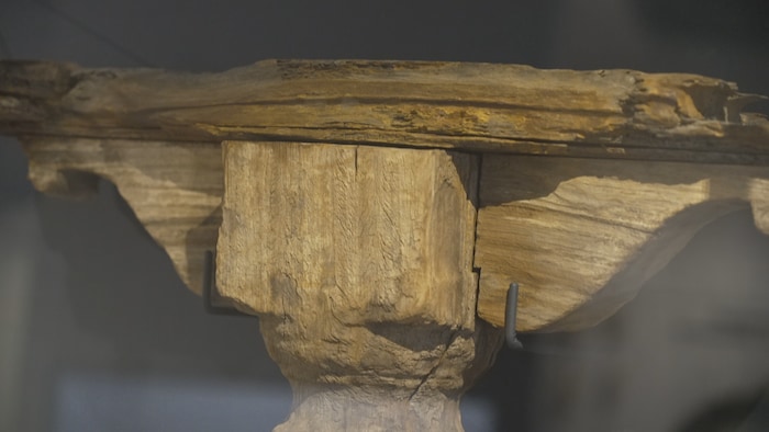 Pied de piano en bois d'acajou exposé derrière une vitre.