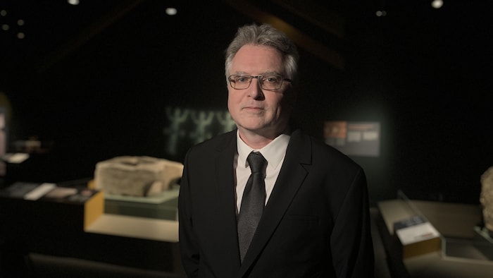 Un homme pose devant des objets antiques dans un musée.