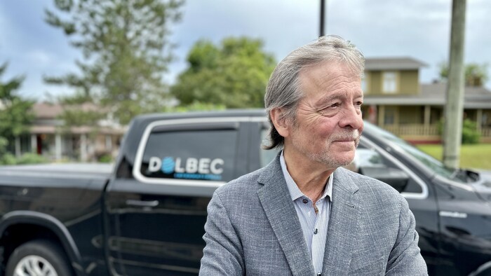 Pierre Dolbec photographié de profil devant une camionnette aux couleurs de son entreprise.