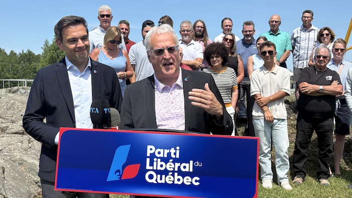Pierre Dufour, debout derrière un lutrin montrant le logo du Parti libéral du Québec, s'adresse aux gens sous le regard de Charles Milliard.