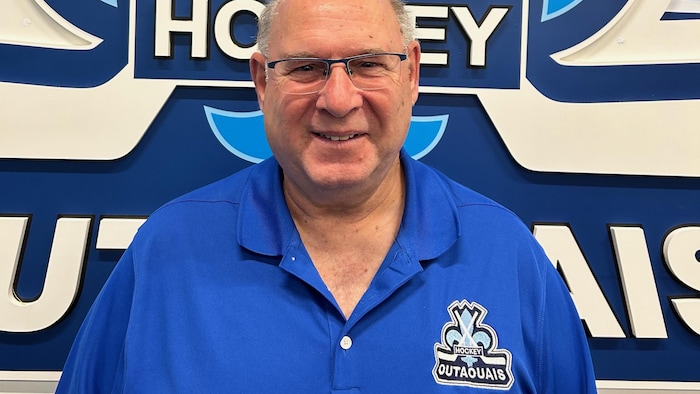 Le président de Hockey Outaouais, Pierre Montreuil devant le logo de l'association.