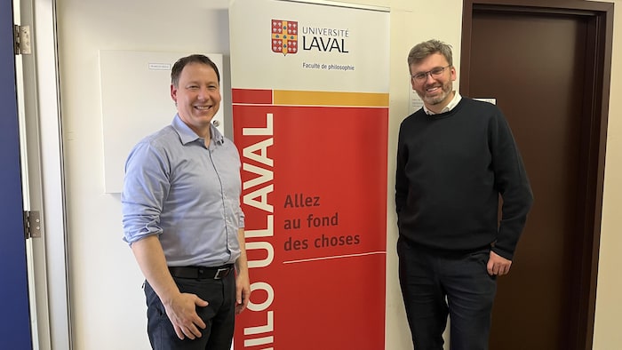 Deux hommes posant devant une bannière de la Faculté de philosophie de l'Université Laval.