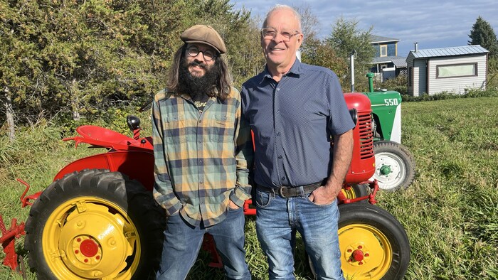 Deux hommes posent devant un tracteur agricole.  
