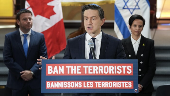 Pierre Poilievre portant une kippa, derrière un lutrin sur lequel connected lit «Bannissons les terroristes».