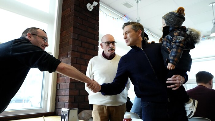 Pierre Poilievre tient son fils et serre la main d'un citoyen.