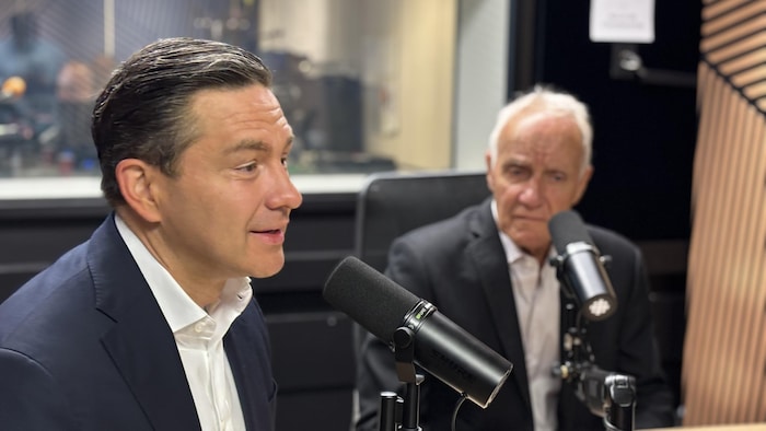 Deux hommes en complet dans un studio de radio. Celui qui est le plus loin de l'objectif apparaît flou.