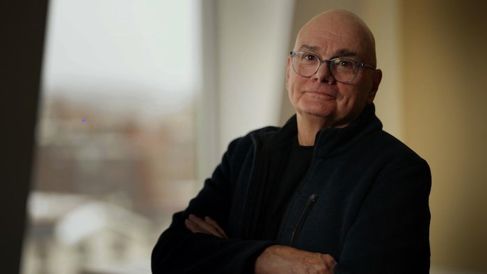 Un homme portant des lunettes prend la pose, les bras croisés, 