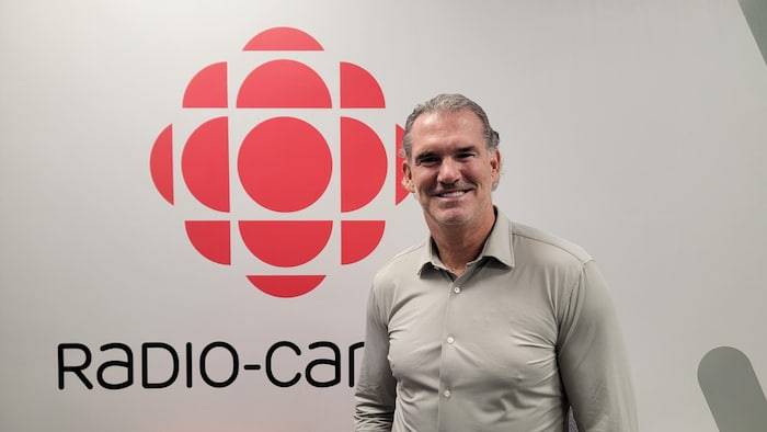 Pierre Turgeon sourit à la caméra en posant près du logo de Radio-Canada.