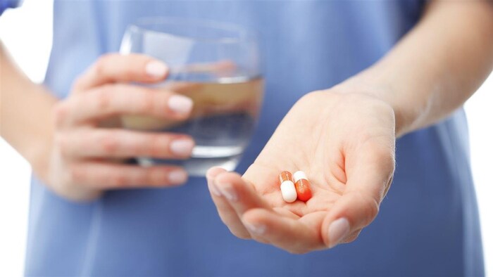 Une femme tient des médicaments dans une main et un verre d'eau dans l'autre. 