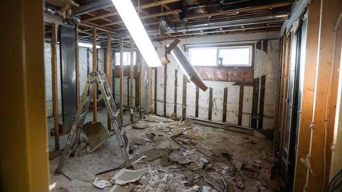 Un escabeau dans un sous-sol jonché de paneaux de gypse en morceaux, dans une maison de Pimicikamak endommagée, le 7 janvier 2026.