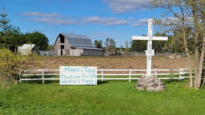 Une affiche est apposée sur une clôture qui entoure une ferme, sur laquelle on peut lire : merci à tous les pompiers, bénévoles, amis et famille.