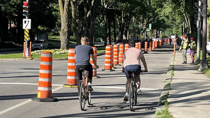 Deux cyclistes sur une voie cyclable temporaire, délimitée par des cônes.