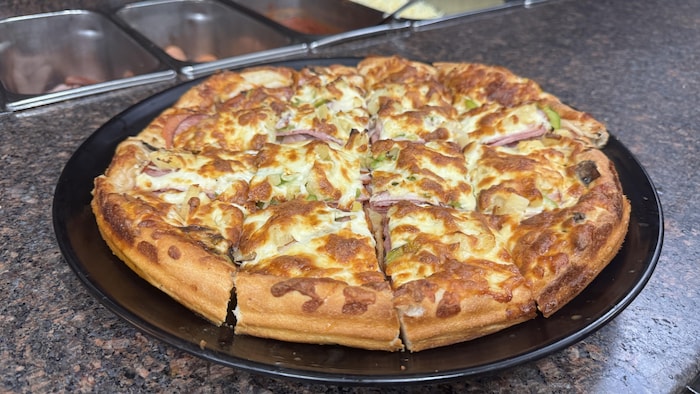 Une pizza réginoise découpée sur un plat avec de la garniture composée entre autres de jambon, d'oignon et de beaucoup de fromage.