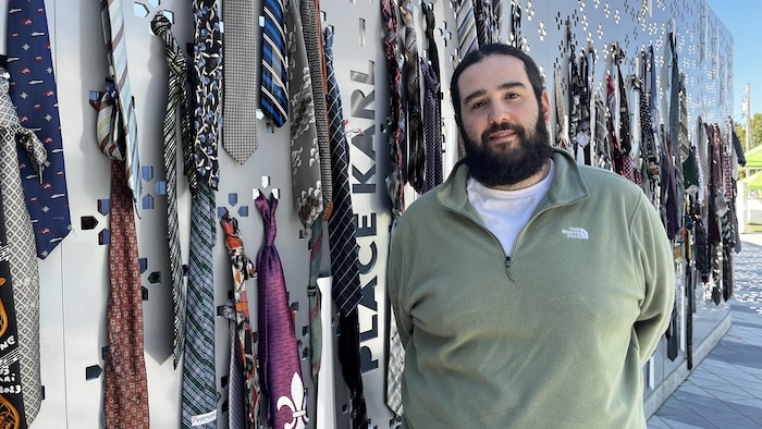 Julien Poissenot-Côté devant le mur de cravates dédié à la mémoire du chanteur Karl Tremblay des Cowboys Fringants décédé en 2023.