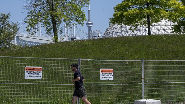 Un coureur passe devant un grillage avec une affiche indiquant que la Place de l'Ontario est en construction.