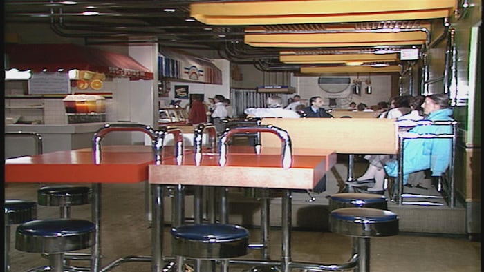 Des clients habillés à la mode des années 1980 attablés.
