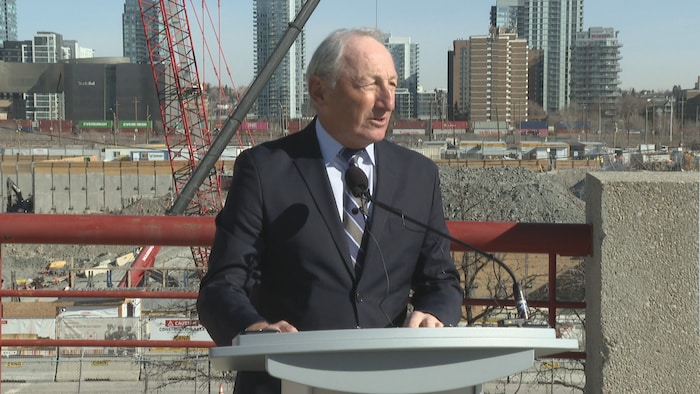 Bob Hunter est debout devant un microphone avec en arrière-plan les travaux en cours.