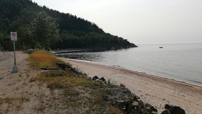 Une pancarte interdisant le stationnement est installée à côté d'un enrochement en bordure d'une plage de sable.