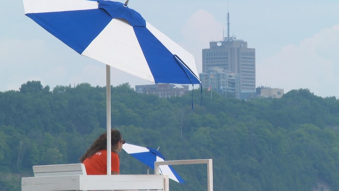 Une sauveteuse sous un parasol regarde au loin.