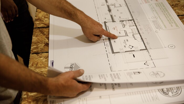 Un homme montre du doigt un plan d'architecte sur un chantier de construction le 6 juillet 2023.