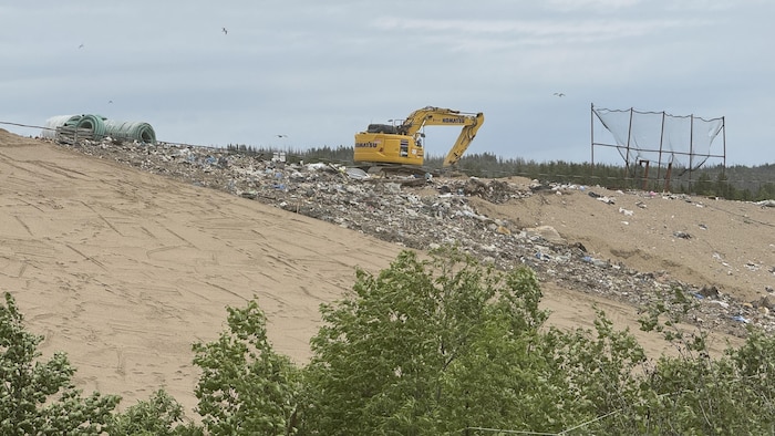 Une pelleteuse travaille en haut d'une colline couverte de déchets.