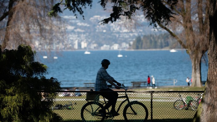 Un homme fait du vélo devant la plage de Kitsilano à Vancouver.