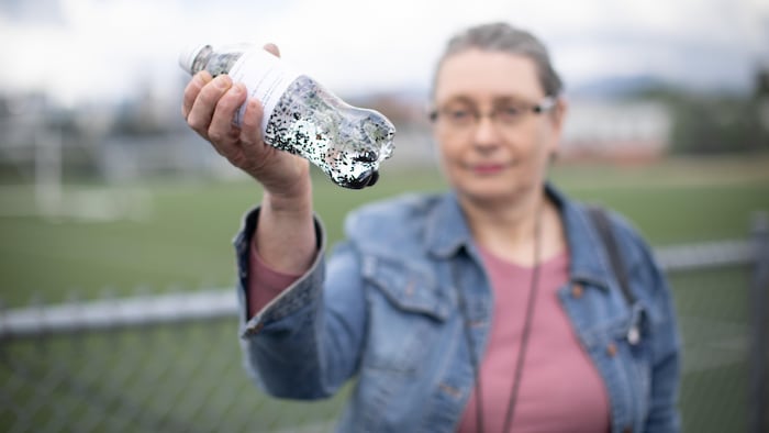 Une femme tient une bouteille avec des granules de caoutchouc.