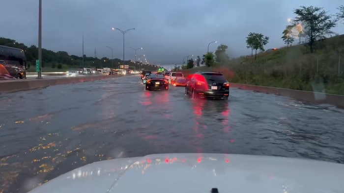 Des véhicules circulent lentement sur une autoroute inondée.