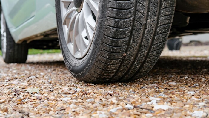 Le pneu d'une voiture stationnée sur un chemin de pierres.