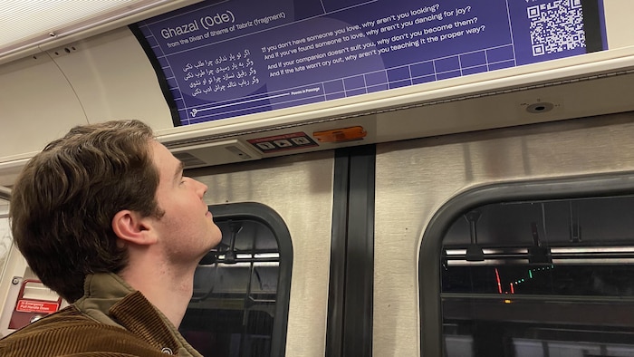Un passager regarde le poème Ghazal (Ode) de Rumi sur un fond mauve dans le métro de Toronto.