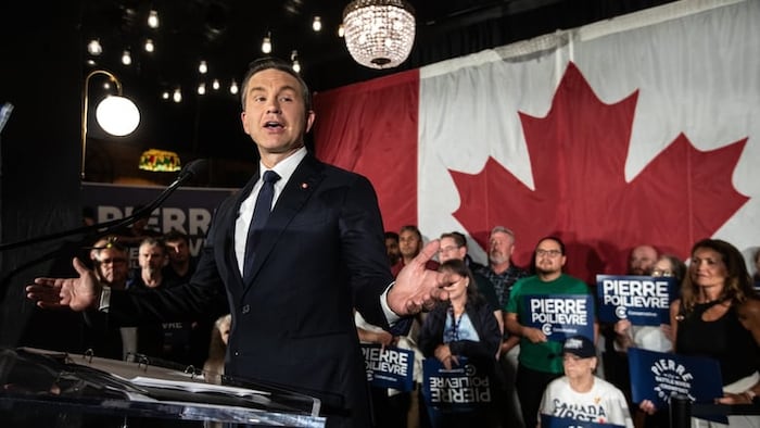 Pierre Poilievre devant un énorme drapeau canadien.