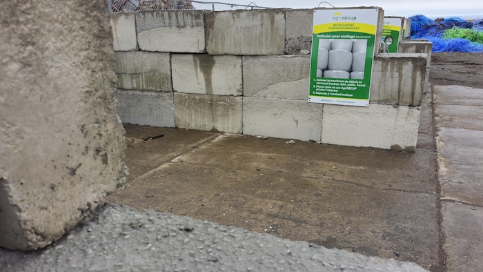 Des structures en blocs de béton avec une affiche AgriRécup et des plastiques colorés à l'arrière-plan.