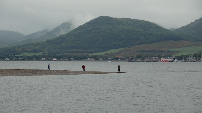 Des pêcheurs sur une pointe de terre entourée d'eau, avec des montagnes à l'arrière.