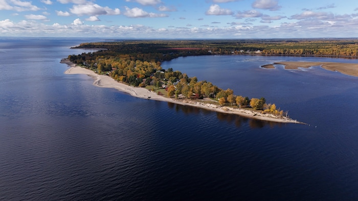 Une vue aérienne montre une étroite presqu'île boisée aux couleurs automnales qui s'avance dans une vaste étendue d'eau bleu foncé.