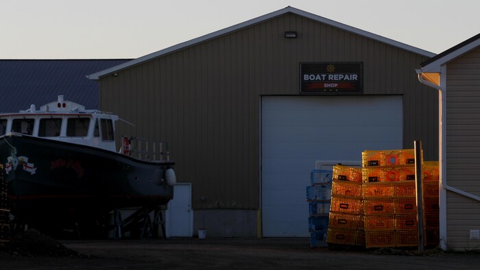Des casiers à homard et un petit bateau devant un entrepôt.