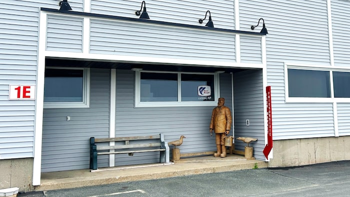 Devant l'entrée d'un bâtiment, une sculpture représentant un pêcheur et deux sculptures plus petites de mouettes montées sur des bûches.