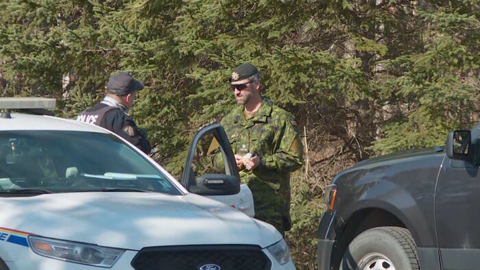 Un policier et un militaire en pleine conversation dehors à côté d'une voiture de police.