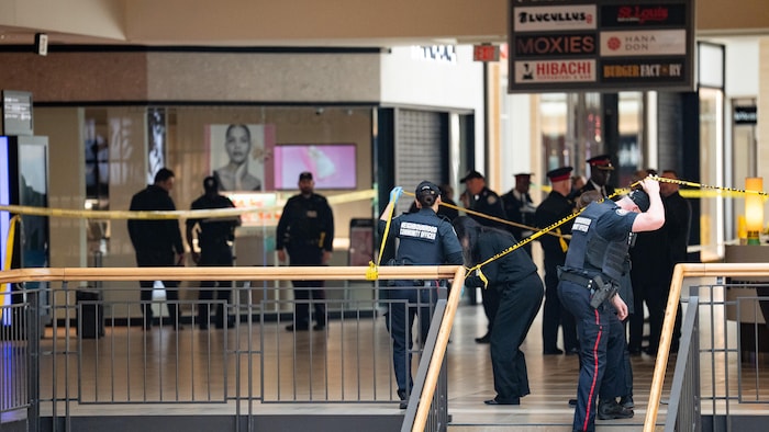Des policiers passent sous un ruban de scène de crime devant une bijouterie.