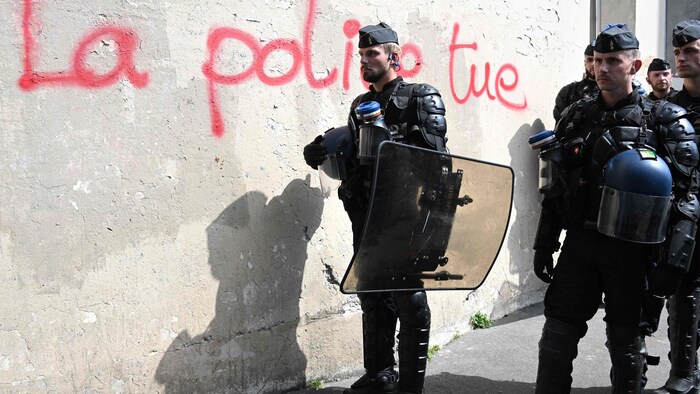 Un policier se tient debout à côté d'un graffiti «La police tue».