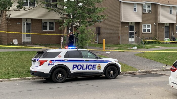 Une voiture de police stationnée devant un périmètre sécurisé après un incident.