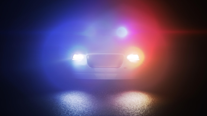 Les gyrophares d'une voiture de police qui s'approche dans la nuit créent des cercles lumineux bleus et rouges.