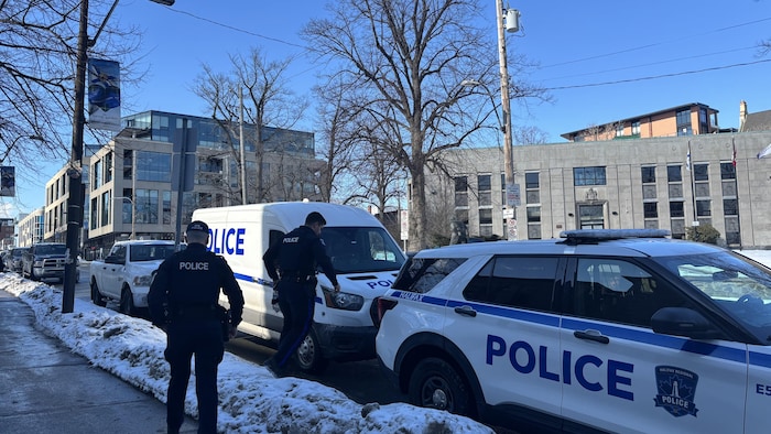 Deux policiers de dos et deux voitures de police. 