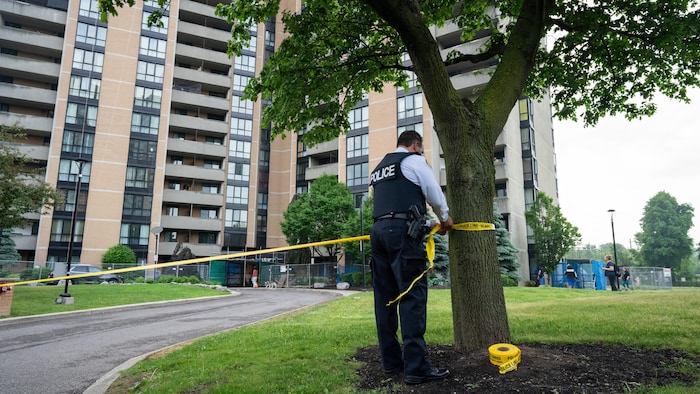 Un agent accroche un ruban de scène de crime autour d'un arbre.