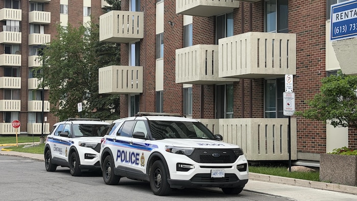 Des voitures de police du service de police d'Ottawa sont stationnées près d'un immeuble de logements.