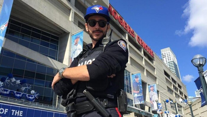 Photo d'un policier en uniforme portant une casquette des Blue Jays devant le stade Rogers.